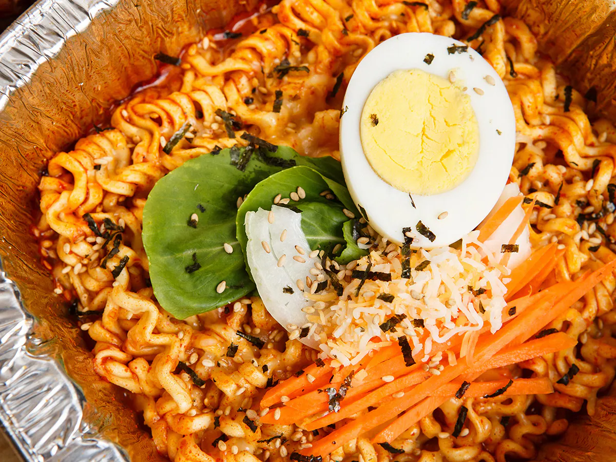 Spicy cheesy stir fire noodles topped boiled egg carrot strips seaweed at JBO Kitchen, an Asian Fusion Restaurant in Pomona